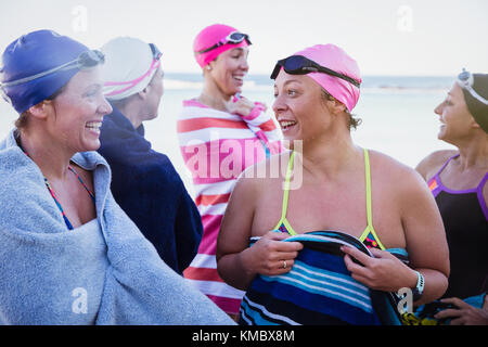 Nuotatori femminili ad acqua aperta che parlano e si asciugano con gli asciugamani sulla spiaggia Foto Stock