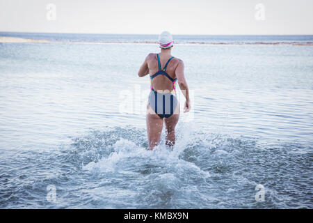 Nuotatore femminile in acqua aperta che corre nel surf oceanico Foto Stock