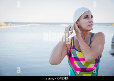 Nuotatore femminile in acqua aperta che regola la cuffia dell'oceano Foto Stock