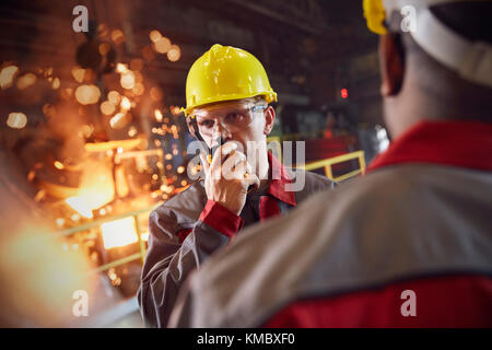 Steelworker che parla, usando walkie-talkie in acciaieria Foto Stock