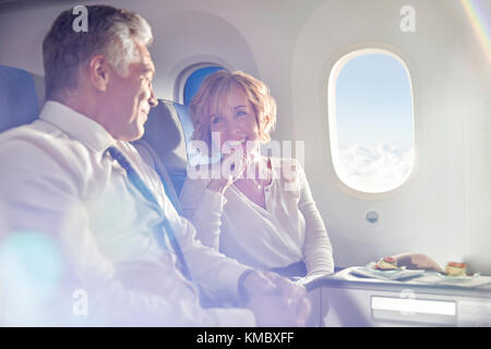 Sorridente coppia matura che mangia e parla in prima classe aereo Foto Stock