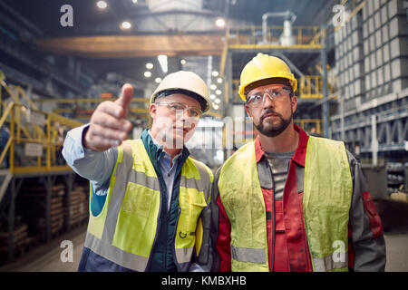 Steelworkers che parlano, gesturing in acciaieria Foto Stock