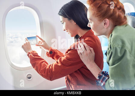 Le giovani donne amici che usano il telefono della macchina fotografica alla finestra dell'aeroplano Foto Stock