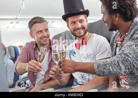 Giovani amici maschi che tostano bicchieri di champagne in aereo Foto Stock