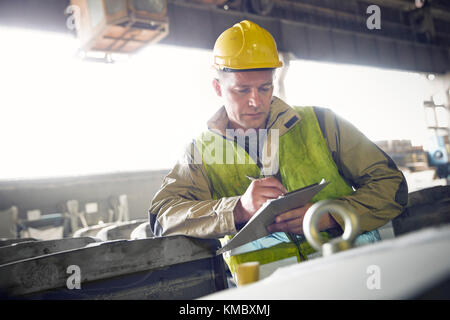 Steelworker scrivere sulla clipboard in acciaieria Foto Stock