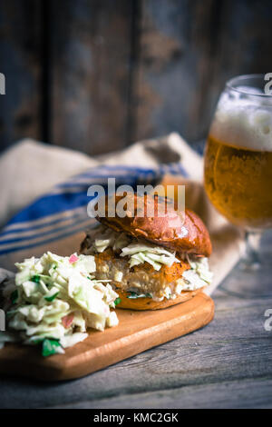 Rustico hamburger di pesce con coleslaw e birra Foto Stock