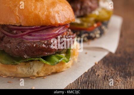 Primo piano di set di tre mini hamburger fatti in casa con manzo di marmo e verdure su un asse di legno. Foto Stock