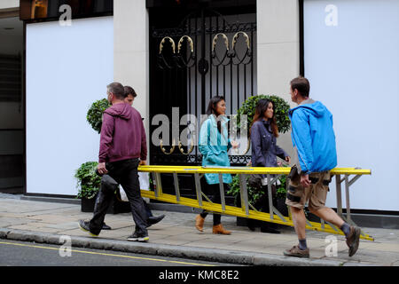 Operai che trasportano un alto scaletta passato gli acquirenti su Old Bond Street, Londra, Inghilterra, Regno Unito Foto Stock