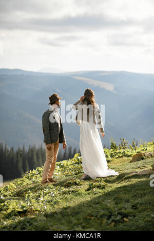 Gli sposi si alzano e guardano in lontananza durante il viaggio in luna di miele nelle montagne dei Carpazi. Vista posteriore. Foto Stock