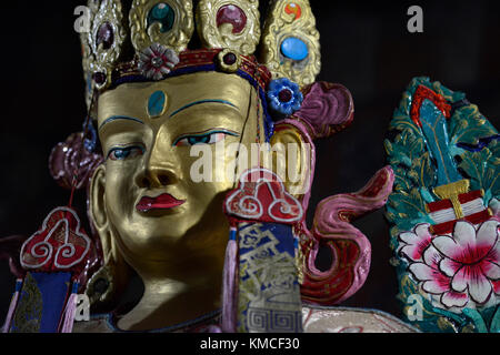 Oro buddha scultura, la faccia decorata con vernici colorate, la corona è decorata con pietre preziose, su uno sfondo nero. Foto Stock