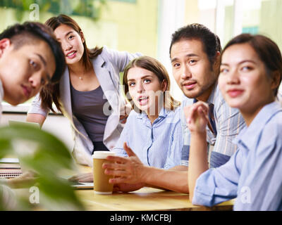 Team di giovani asiatici e caucasici imprenditori maschio e femmina di riunione in ufficio. Foto Stock