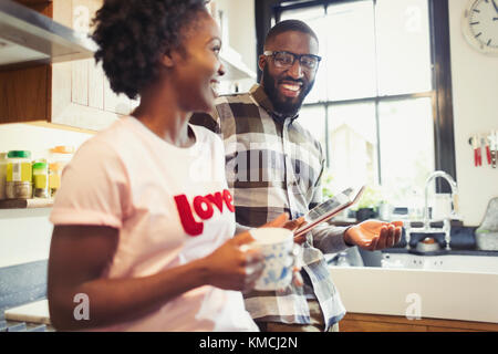 Giovane coppia che beve caffè e usa un tablet digitale in cucina Foto Stock