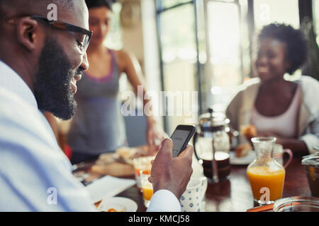 Giovane uomo testando con smartphone al tavolo da cucina Foto Stock