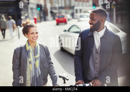 Una coppia sorridente che si spostava in bicicletta su una strada urbana soleggiata Foto Stock