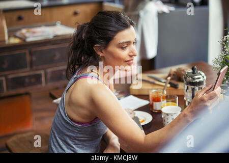 Giovane donna che testava con lo smartphone al tavolo della colazione Foto Stock