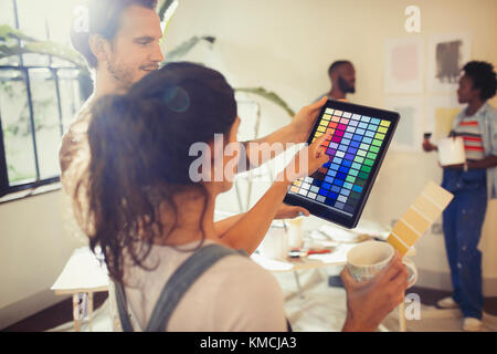 Amici con tablet digitale che guardano campioni di vernice digitale, dipingendo il salotto Foto Stock
