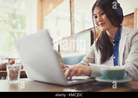 Giovane donna che usa un computer portatile e beve caffè al bar Foto Stock
