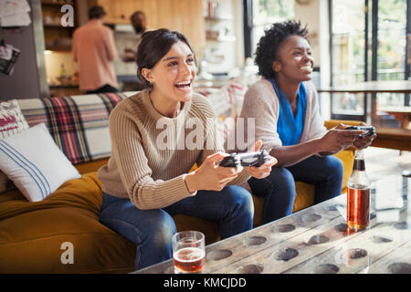 Ridendo amici donne che giocano a videogiochi sul divano del soggiorno Foto Stock