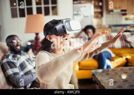 Donna gesturing, utilizzando occhiali simulatore di realtà virtuale in soggiorno Foto Stock