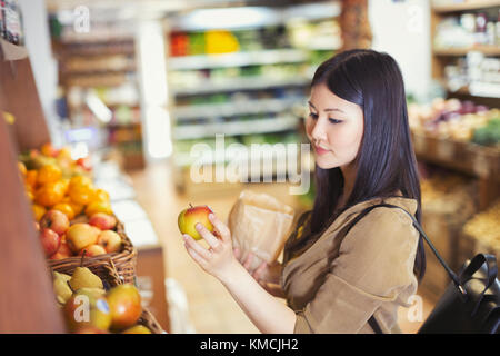 Giovane donna che acquista, esaminando la mela nel negozio di alimentari Foto Stock