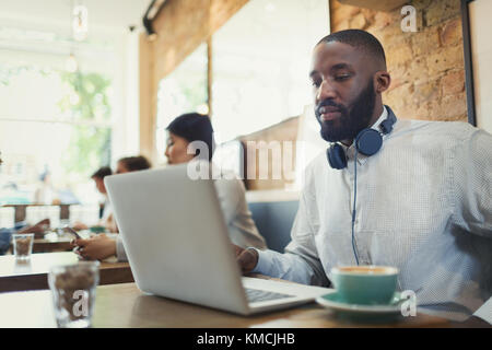Giovane uomo con le cuffie che usano il computer portatile e che beve il caffè caffè Foto Stock