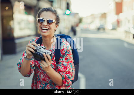 Ritratto ridendo, entusiasta giovane turista in occhiali da sole fotografando con la macchina fotografica su strada urbana Foto Stock