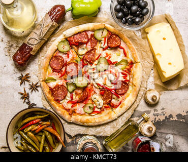 Pizza di carne con ingredienti intorno al formaggio, salsiccia per pizza, carne, olive, peperoni, funghi e spezie. su sfondo rustico. vista superiore Foto Stock