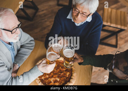 Senior amici tintinnanti bicchieri di birra Foto Stock