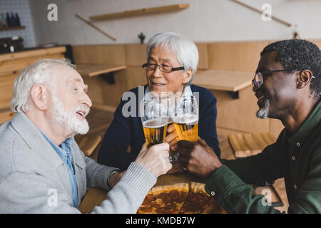 Senior amici tintinnanti bicchieri di birra Foto Stock