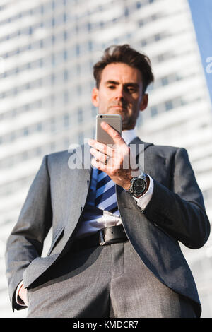 Ritratto di un imprenditore che si erge nella parte anteriore di un grattacielo e gestisce un telefono cellulare Foto Stock