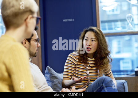 Asian imprenditrice avente una discussione con i colleghi del Caucaso in un ufficio contemporaneo Foto Stock