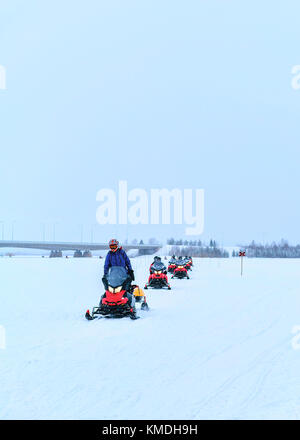 Persone a cavallo delle motoslitte sul lago ghiacciato in inverno rovaniemi, Lapponia, Finlandia Foto Stock