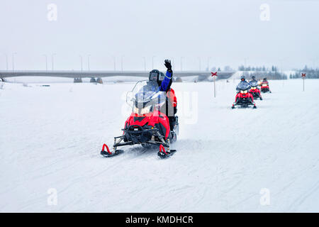 Persone a cavallo delle motoslitte e agitando le mani sul lago ghiacciato in inverno rovaniemi in Lapponia, Finlandia Foto Stock