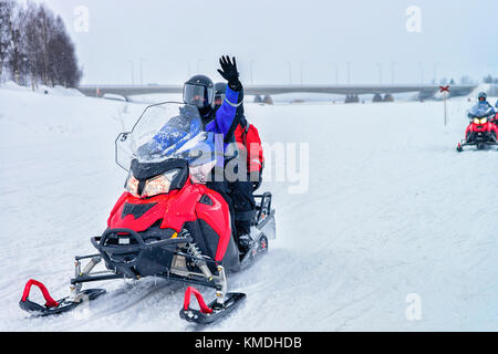 Persone a cavallo delle motoslitte e agitando le mani sul lago ghiacciato in inverno rovaniemi, Lapponia, Finlandia Foto Stock