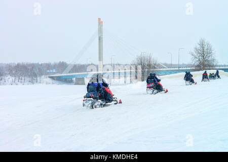 Persone a cavallo delle motoslitte a candela ponte sul lago ghiacciato in inverno rovaniemi, Lapponia, Finlandia Foto Stock