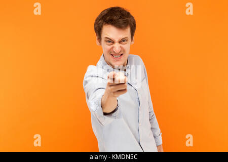 Hey! Uomo pazzo puntare il dito alla telecamera. Studio shot, sfondo arancione Foto Stock