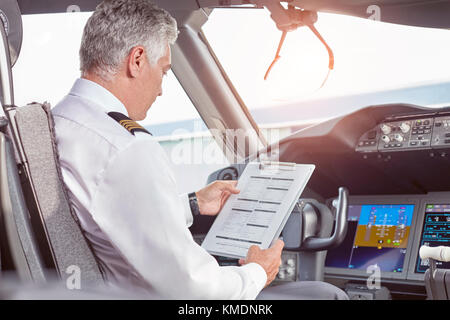 Pilota maschio con la preparazione degli appunti in aereo cockpit Foto Stock