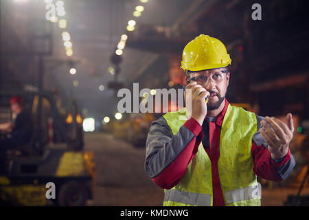 Steelworker che parla, usando walkie-talkie in acciaieria Foto Stock