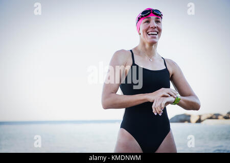 Nuotatore sorridente in acqua aperta che regola l'orologio intelligente sull'oceano Foto Stock