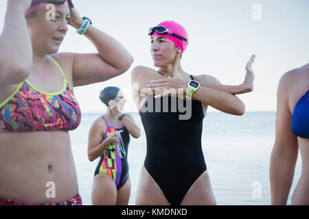 Nuotatori femminili in acqua aperta con orologio intelligente che stretching e preparazione Foto Stock