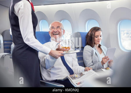 Assistente di volo che serve il whiskey a sorridente uomo d'affari che cavalcano in primo luogo classe in aereo Foto Stock