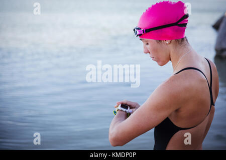 Nuotatore femminile in acqua aperta che controlla l'orologio intelligente all'oceano Foto Stock