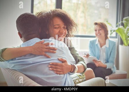 Sorridente terapeuta femminile che guarda la coppia abbracciare nella sessione di terapia delle coppie Foto Stock