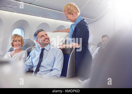 Sorridente assistente di volo cuscino di regolazione per l'imprenditore in prima classe in aereo Foto Stock