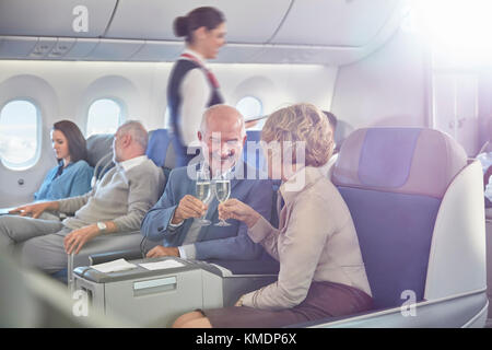 Coppia matura che tosta bicchieri di champagne in prima classe in aereo Foto Stock