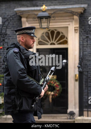 Un agente di polizia armato passeggiate oltre la porta di 10 Downing Street a Londra. Naa'imur Zakariyah Rahman è apparso a Westminster Magistrates Court accusato di cospirazione per assassinare il PM in una bomba a orologeria e attacco di coltello a Downing Street. Foto Stock