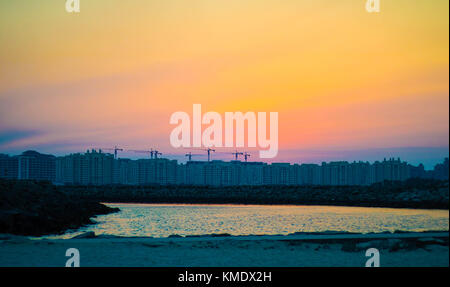 Una vista degli edifici di Dubai al di sopra del cielo arancione durante un tramonto dalla spiaggia. Foto Stock