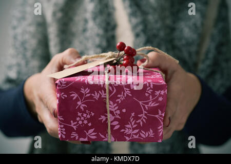 Primo piano di una giovane donna caucasica tenendo un dono nelle sue mani avvolte in una carta di Nizza, legata con una stringa di rustico e ornata con finti holly Foto Stock