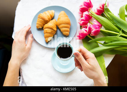 Ragazza con croissant e caffè, un bouquet di tulipani rosa, mattina felice Foto Stock