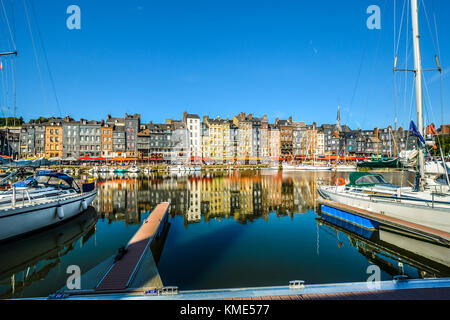 Una fila di case, aziende e caffetterie riflettono l'acqua presso il molo vecchio di Honfleur Francia sulla costa della Normandia Foto Stock